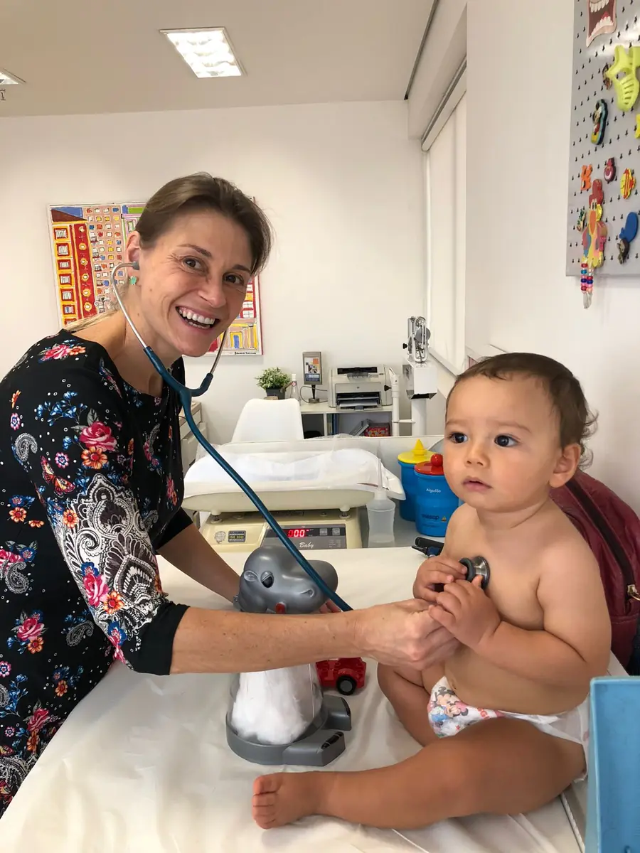 Dra. Milena examinando bebê com estetoscópio, sorrindo