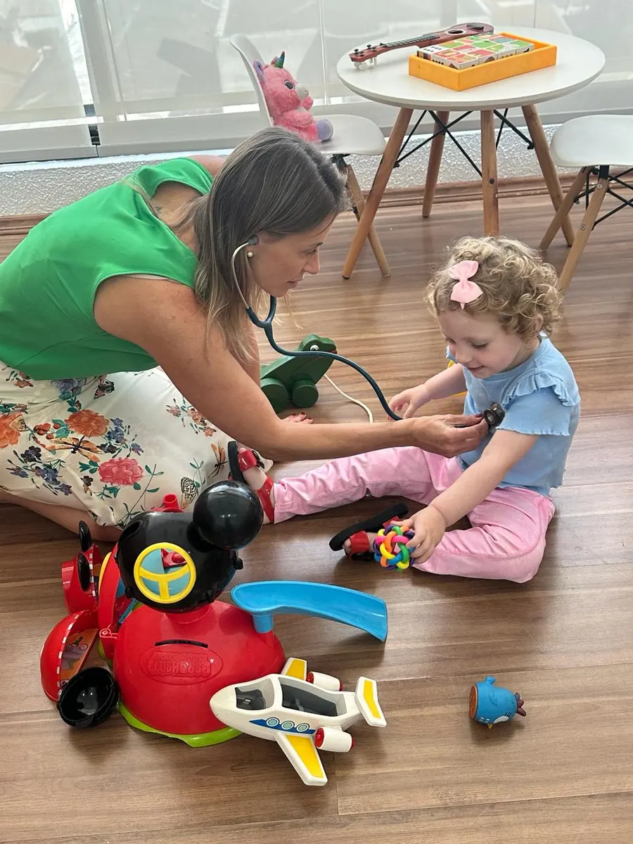 Dra. Milena brincando no chão durante consulta com criança
