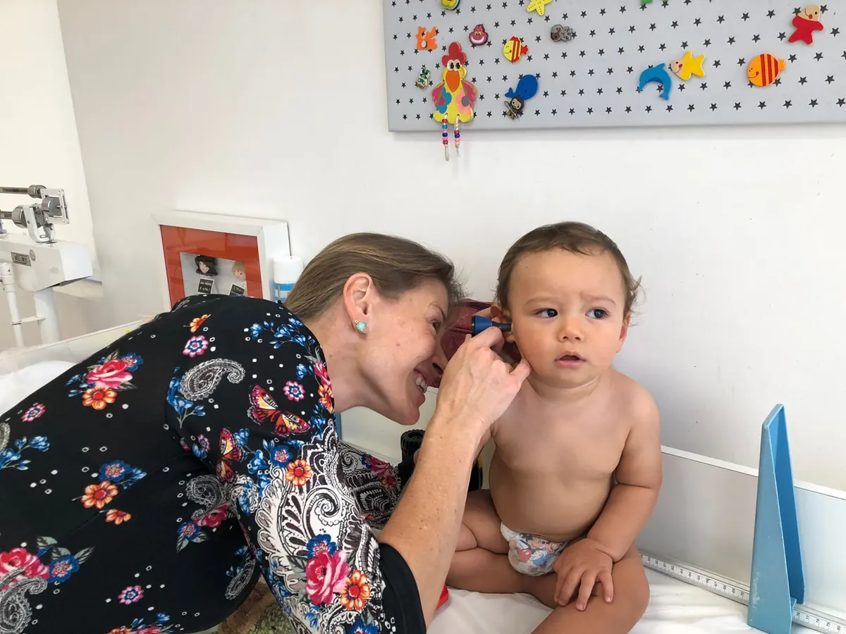 Dra. Milena examinando ouvido de bebê com otoscópio